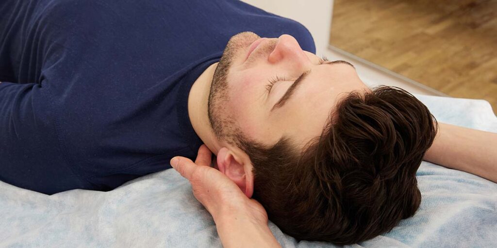 Osteopathin behandelt Nacken und oberen Brustkorb eines Patienten mit Kopfschmerzen